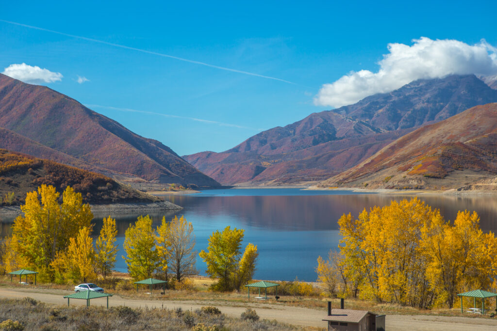 A tranquil day at Deer Creek Reservoir with activities like paddleboarding, jet-skiing, windsurfing, and hiking trails, all surrounded by beautiful nature.